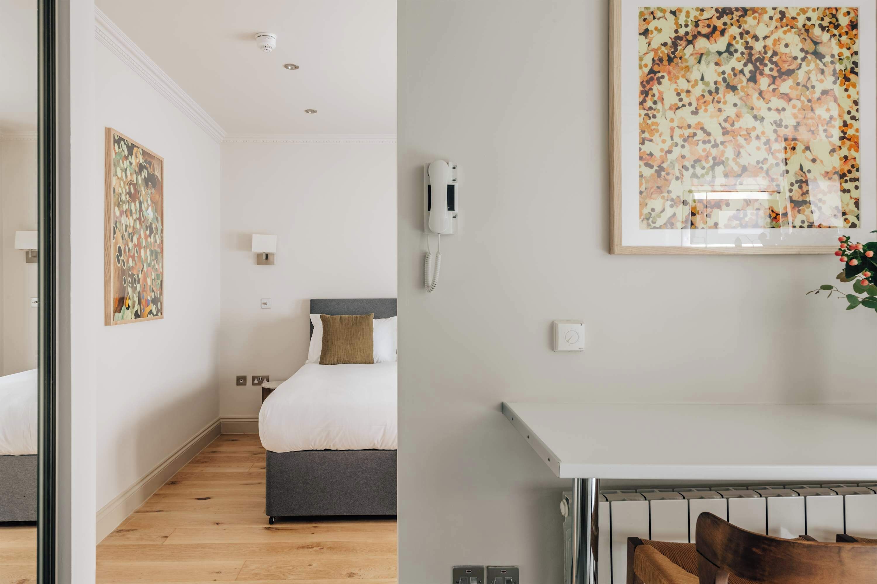 Habitación de hotel con cama, mesita de noche, teléfono en la pared y una obra de arte.