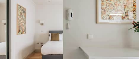 A hotel room with a bed, bedside table, wall-mounted phone, and artwork.