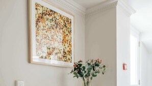 En matplats med ett vitt bord, två trästolar, en vas med blommor och ett inramat konstverk på väggen.
