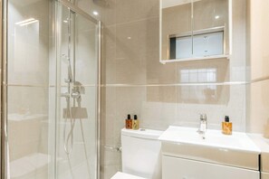 A modern bathroom with a glass-enclosed shower, a white sink with a mirror above it, and toiletries on the counter.