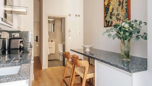 Une cuisine moderne avec un plan de travail en granit, des tabourets de bar en bois, un vase agrémenté de plantes et un tableau accroché au mur.