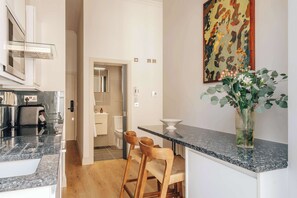 Eine moderne Küche mit einer Granitabdeckung, Holzhocker, einer Vase mit Grünpflanzen und einem Bild an der Wand.