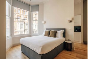 Ein Schlafzimmer mit Bett, Fenster, Nachttisch und Blick auf Gebäude.
