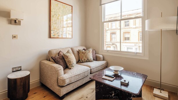 Un salon moderne comprenant un canapé, une table basse en marbre, une lampe sur pied, un tableau et une fenêtre donnant sur des immeubles.