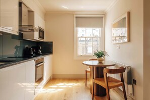 Eine moderne Küche mit weißen Schränken, einer schwarzen Arbeitsplatte und einem eingebauten Backofen. Ein Fenster bietet Blick auf Gebäude.