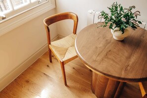 A wooden dining table with a woven chair and a potted plant. - The Cheniston by nestor | Kensington Studio (London)
