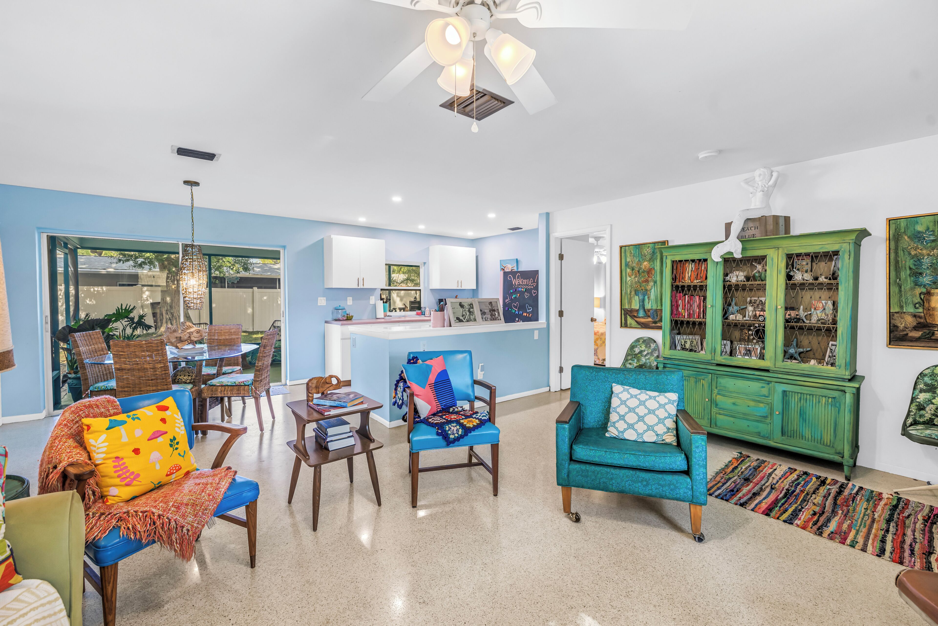 A living room with a blue sofa, a green cabinet, and a dining area with wicker furniture.
