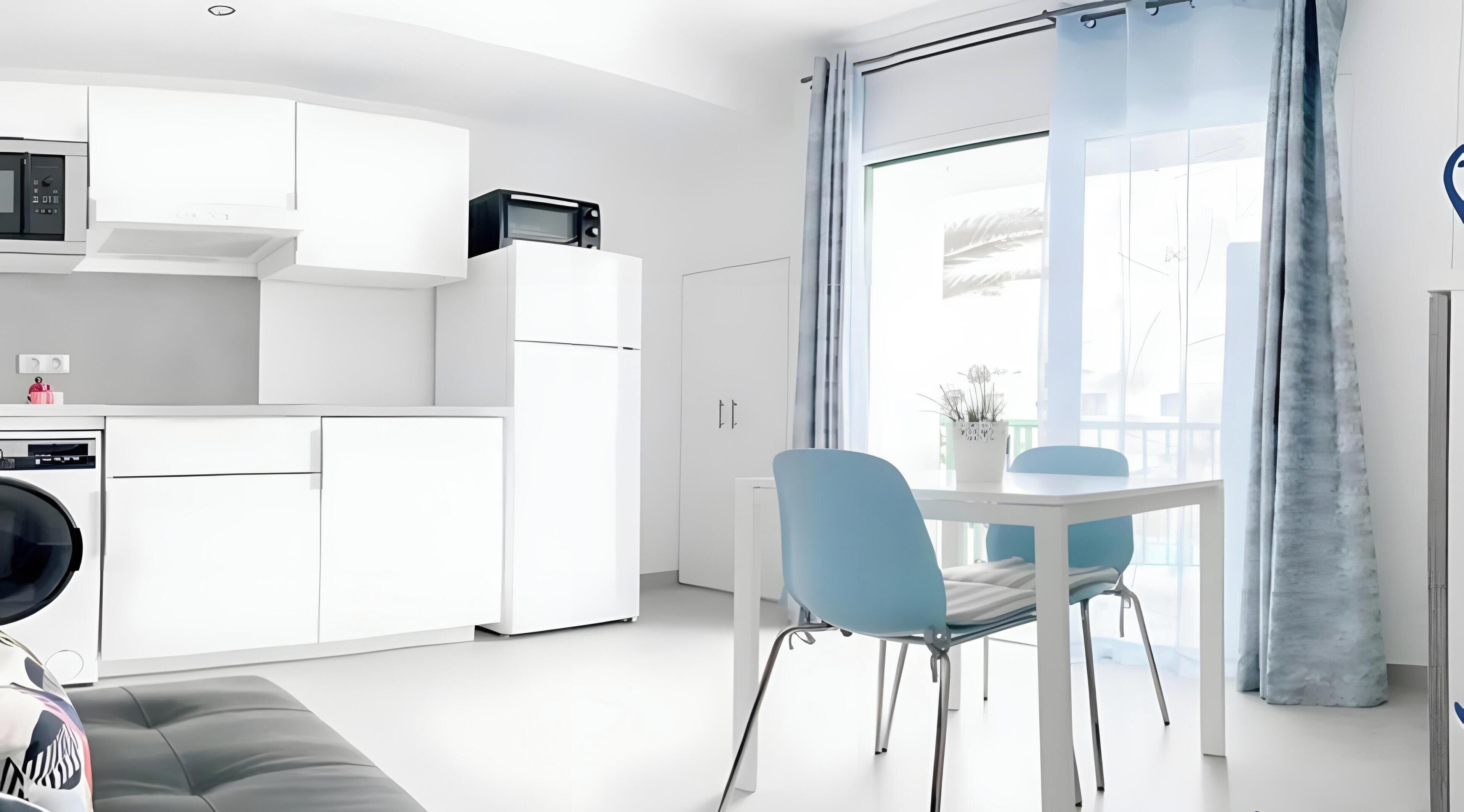 Una cocina moderna con armarios blancos, un microondas y un comedor con mesa y sillas.