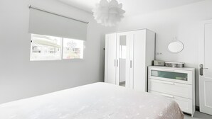 Une chambre à coucher avec un grand lit, une armoire, une commode et une fenêtre donnant sur un immeuble.