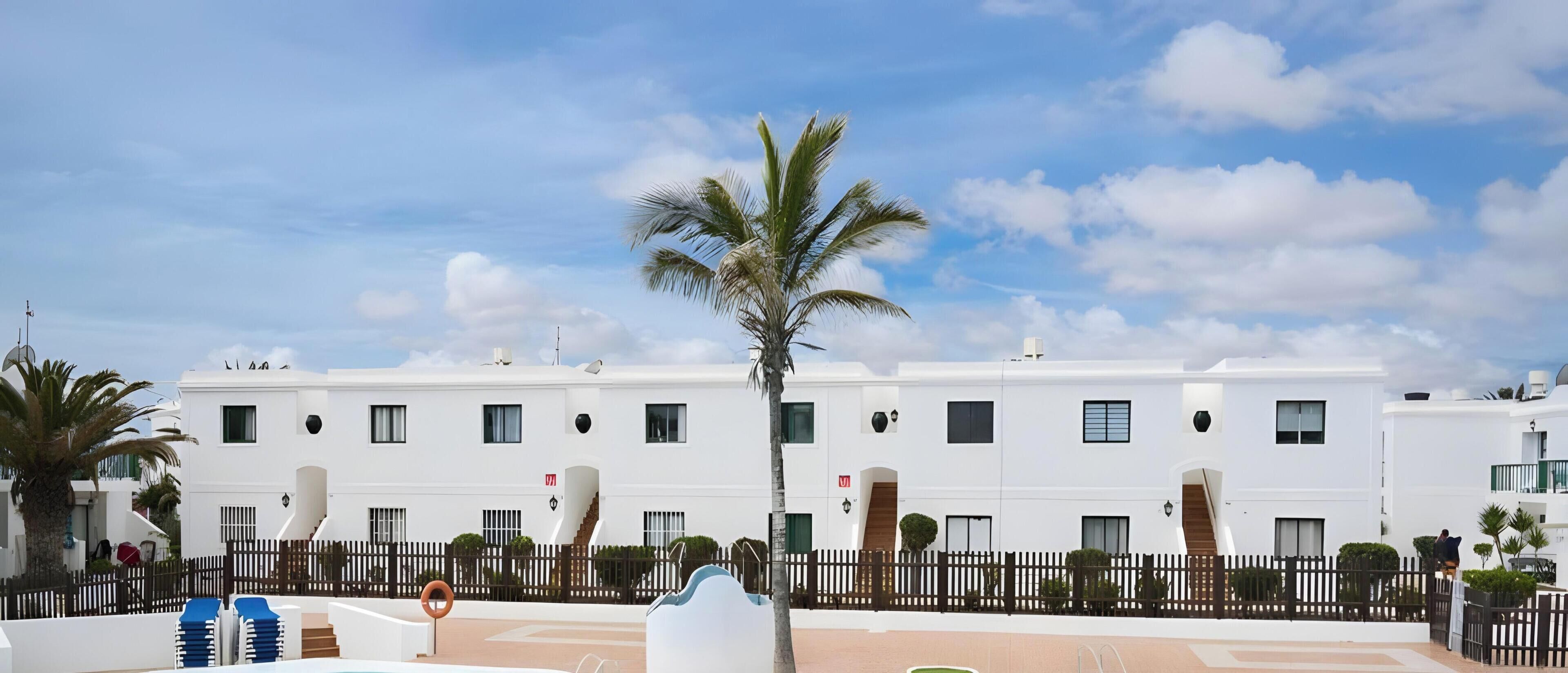 Un bâtiment blanc avec de nombreuses fenêtres et un palmier devant.