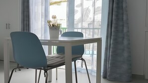 Une pièce moderne avec une table et des chaises, une plante en pot et une grande fenêtre ornée de rideaux légers.