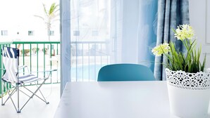 Un balcon avec une table blanche, une chaise bleue, un pot de fleurs aux fleurs jaunes et une rambarde verte.