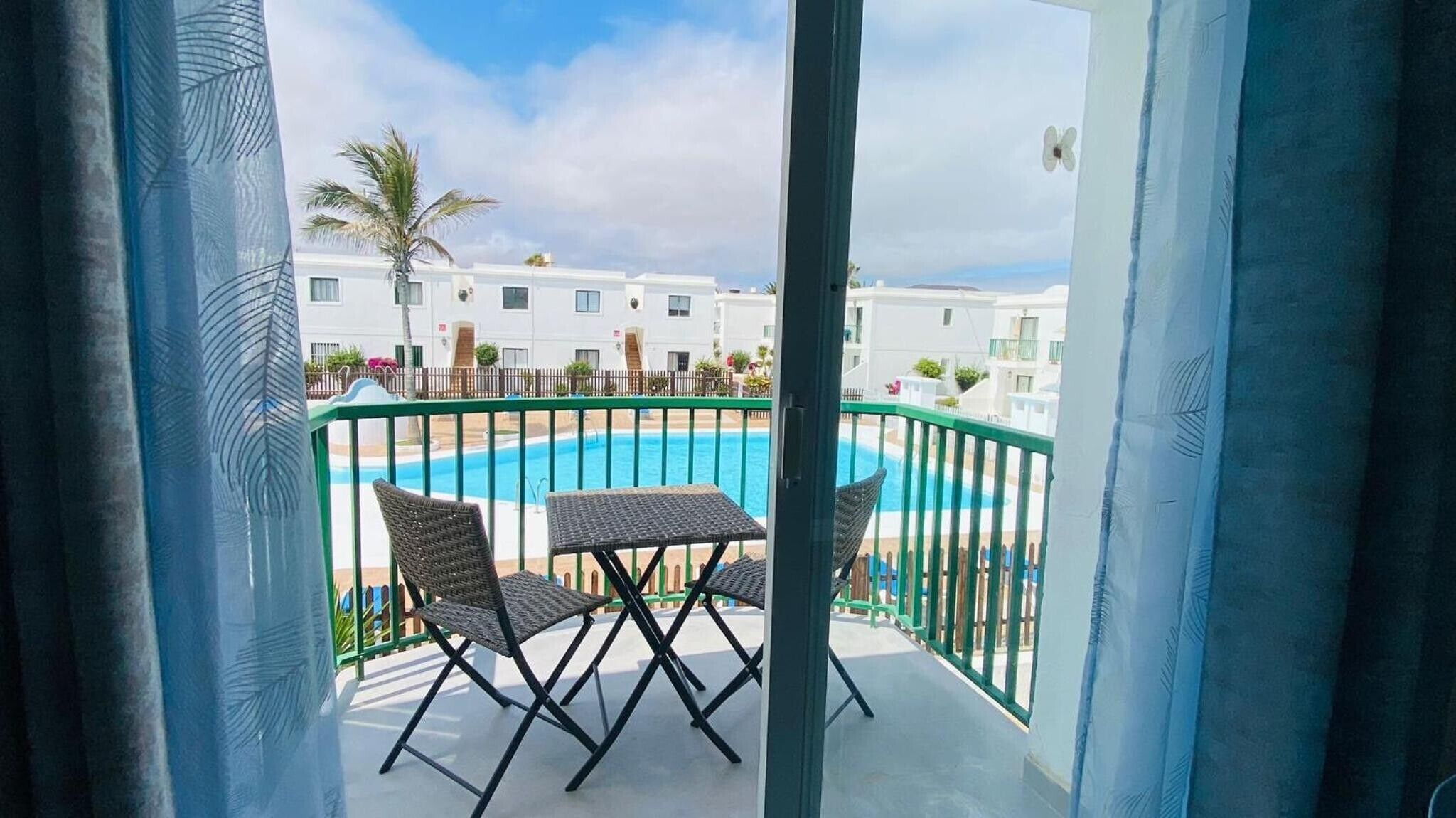 Ein Balkon mit Pool, Korbstühlen und Blick auf einen weißen Gebäudekomplex.