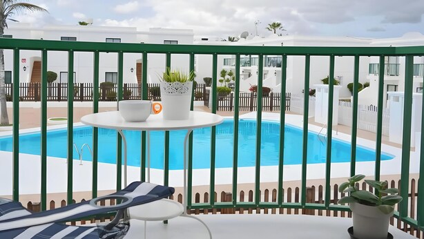 Une vue sur la piscine, avec une balustrade verte, des chaises longues et une table sur laquelle se trouvent un saladier et une plante.