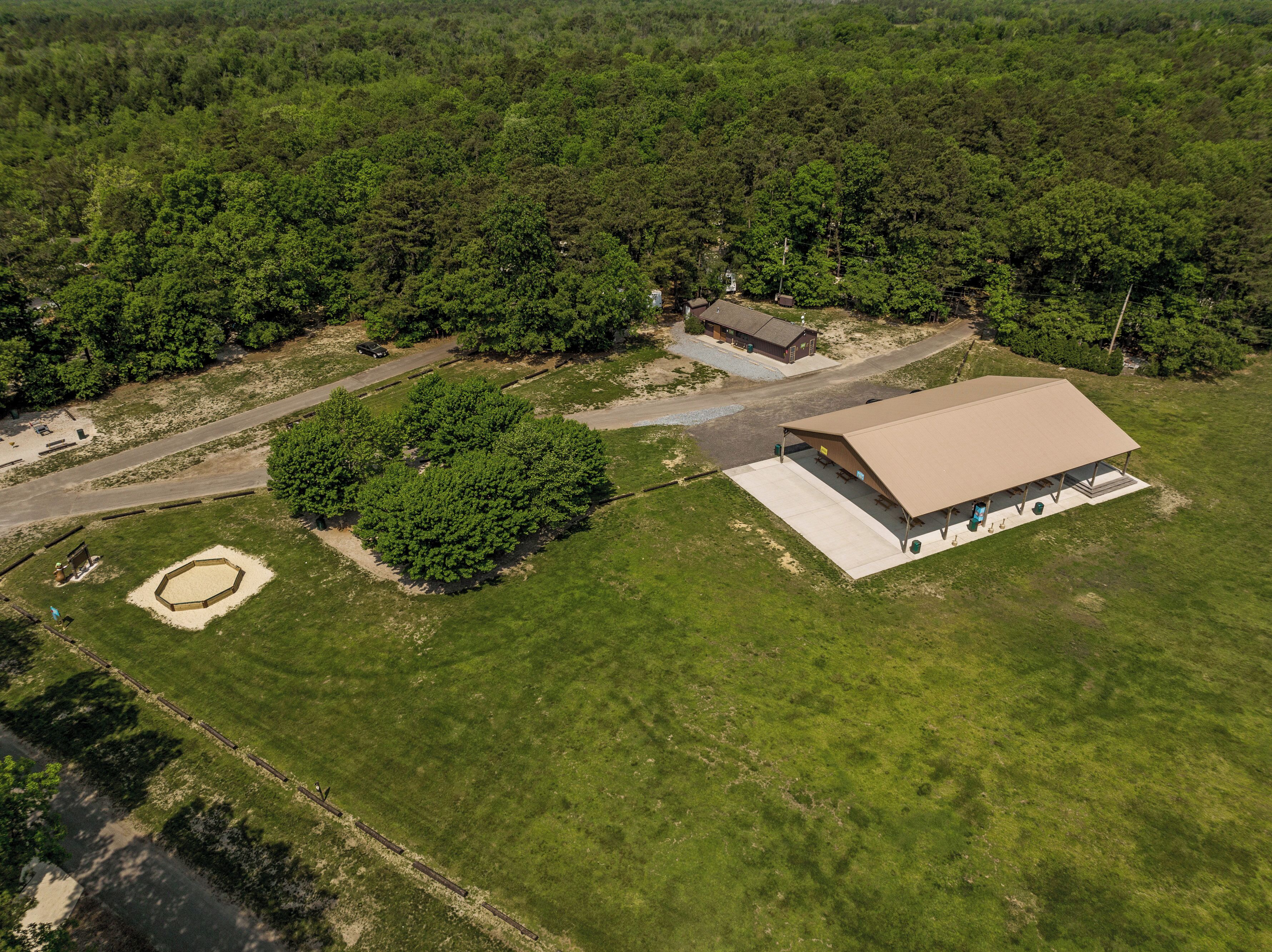 An aerial view of a property with a large covered outdoor area, a small building, and a dirt path.