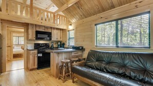 A cabin interior with a kitchen, dining area, and a living room with a leather couch. - Sun Retreats Hospitality Creek (Monroe)