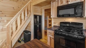 A compact kitchen with wooden walls, a microwave, a stove, and a refrigerator. - Sun Retreats Hospitality Creek (Monroe)