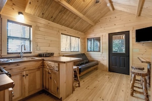Interior de una cabaña con cocina, un sofá y una puerta.