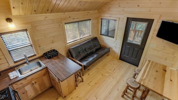 A compact kitchen with a sink, stove, and wooden cabinets. There is a black leather sofa and a small dining area with stools.