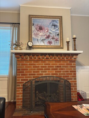 A fireplace with a brick surround, a framed floral artwork above it, a clock, and two candle holders.