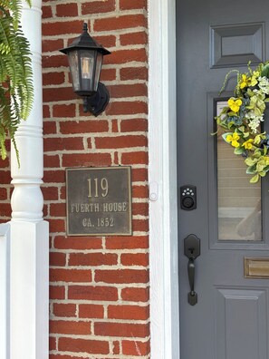 A brick house with a number plaque, a doorbell, and a flower wreath.