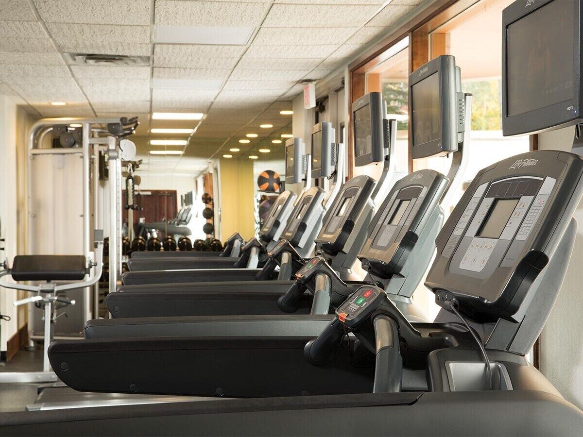 A row of treadmills in a gym with exercise equipment and a TV screen.