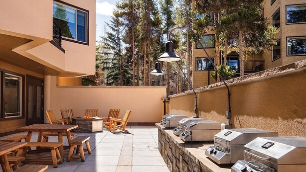 En uteplats med träbord och stolar, en grill och en mur av sten.