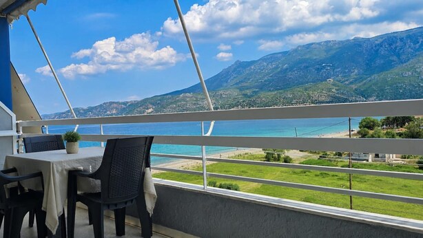A balcony with a table and chairs, overlooking a coastal landscape with mountains in the distance. - Esperides Pearl Luxury SeaView Apartment by DM Hospitality (LOUTRAKI)