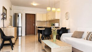 A modern living room with a sofa, a coffee table, and a dining area with chairs and a table. - Esperides Pearl Luxury SeaView Apartment by DM Hospitality (LOUTRAKI)