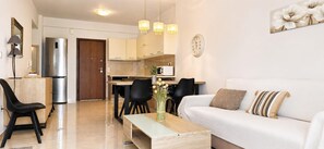 A modern living room with a sofa, a coffee table, and a dining area with chairs and a table. - Esperides Pearl Luxury SeaView Apartment by DM Hospitality (LOUTRAKI)