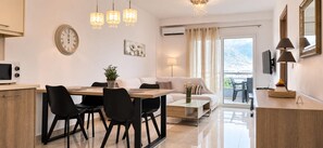 A modern living space with a dining area, a sofa, a coffee table, and a balcony with a view. - Esperides Pearl Luxury SeaView Apartment by DM Hospitality (LOUTRAKI)