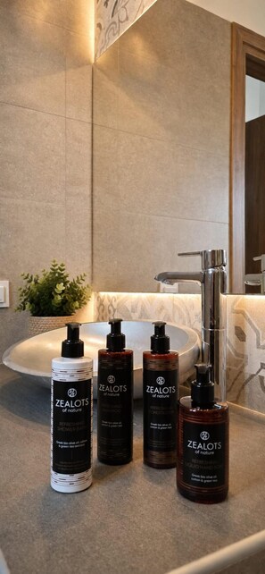 Un baño con un lavamanos moderno, un espejo y cuatro botellas de productos Zealots of Nature.