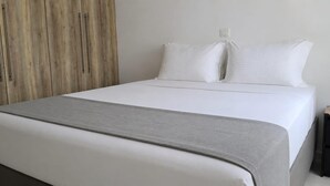 A neatly made bed with a grey throw blanket, a wooden wardrobe, and a bedside table with a lamp. - Esperides Pearl Luxury SeaView Apartment by DM Hospitality (LOUTRAKI)