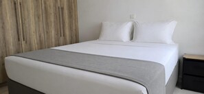 A neatly made bed with a grey throw blanket, a wooden wardrobe, and a bedside table with a lamp. - Esperides Pearl Luxury SeaView Apartment by DM Hospitality (LOUTRAKI)