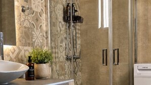 A modern bathroom with a glass-enclosed shower, a sink with a basin, a potted plant, and a washing machine. - Esperides Pearl Luxury SeaView Apartment by DM Hospitality (LOUTRAKI)