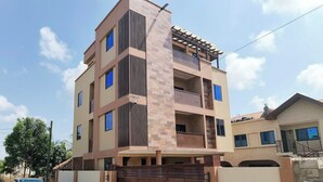 Un edifici residencial de diversos pisos amb una entrada tancada per reixa, un vehicle estacionat i un cel serè.