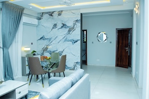 Una sala de estar moderna con una pared de mármol, un comedor con mesa de vidrio y un sofá.