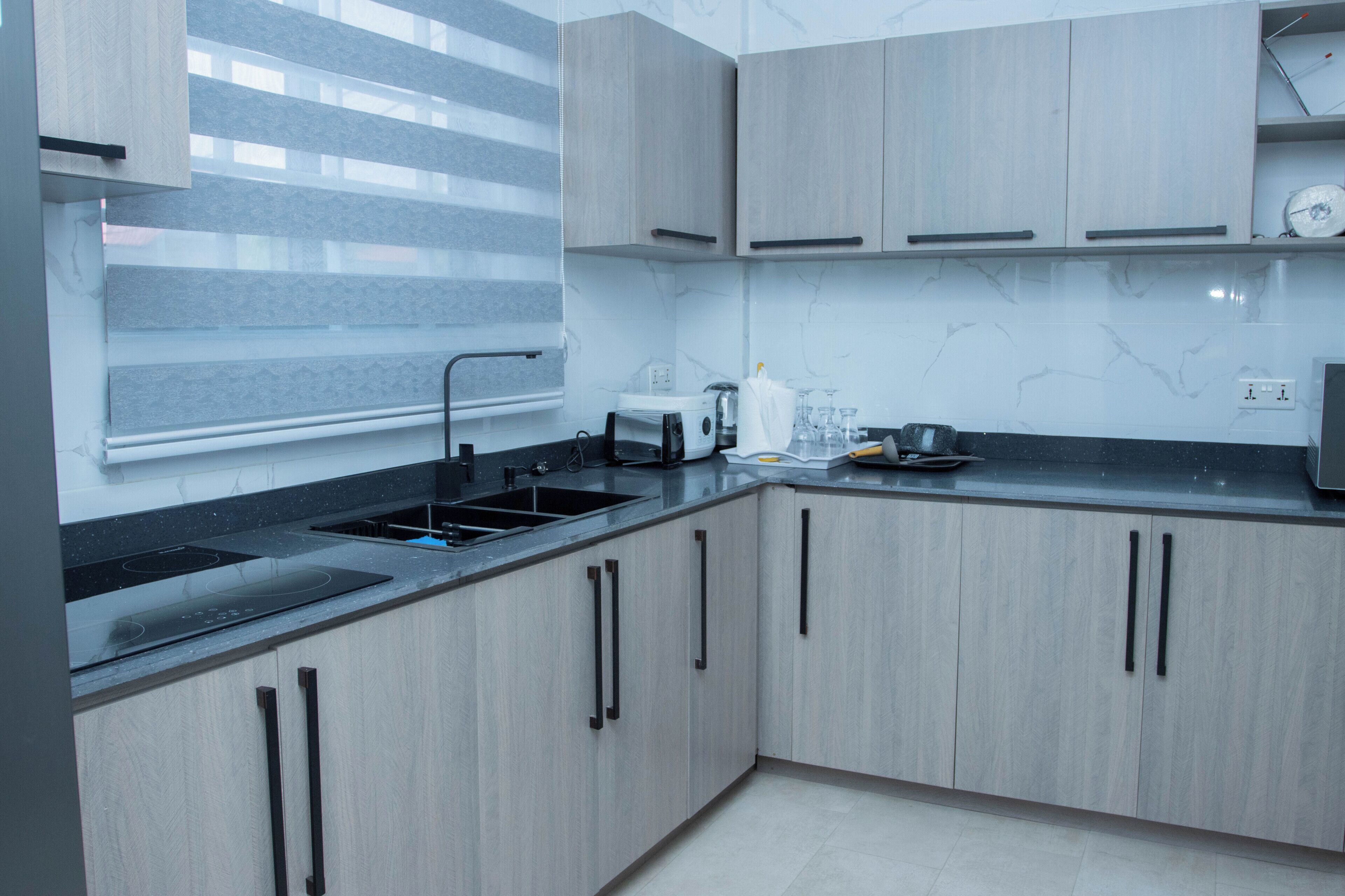 A modern kitchen with grey cabinets, a black countertop, and a window with blinds.