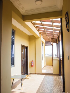 A corridor with a wooden ceiling, a fire extinguisher, a door, and a view through an open window. - The Beniluxe (Accra)