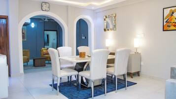 Un comedor con una mesa blanca, cuatro sillas, un tapete azul y un reloj en la pared.
