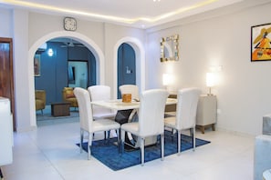 Un comedor con una mesa blanca, cuatro sillas, un tapete azul y un reloj en la pared.