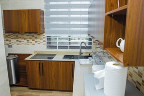 Cocina compacta con muebles de madera, un lavamanos de acero inoxidable y una ventana con persianas.