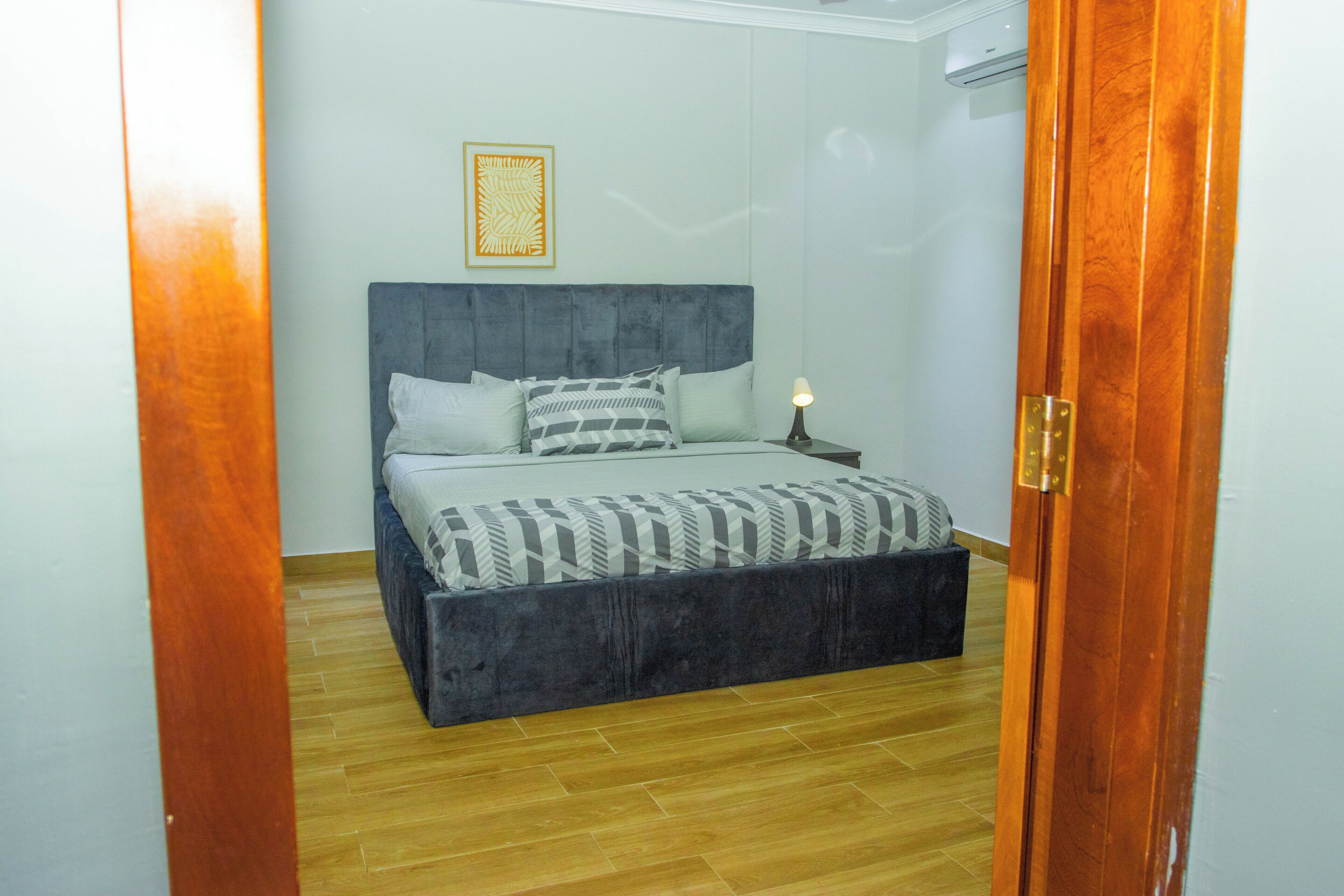A bedroom with a bed, a nightstand, a wall-mounted air conditioner, and a wooden door frame.