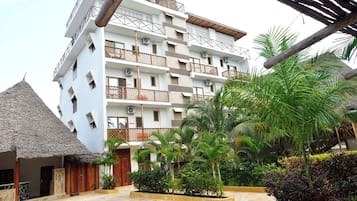 Ein mehrstöckiges Hotel mit Balkonen, einem Gebäude mit Strohdach und üppiger tropischer Bepflanzung.
