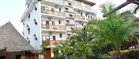 A multi-story hotel with balconies, a thatched-roof structure, and lush tropical landscaping.