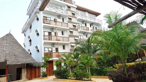 A multi-story hotel with balconies, a thatched-roof structure, and lush tropical landscaping. - Maji Pearl Hotel & Spa (Nungwi)