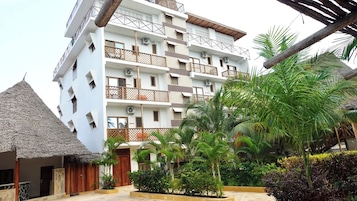 A multi-story hotel with balconies, a thatched-roof structure, and lush tropical landscaping.