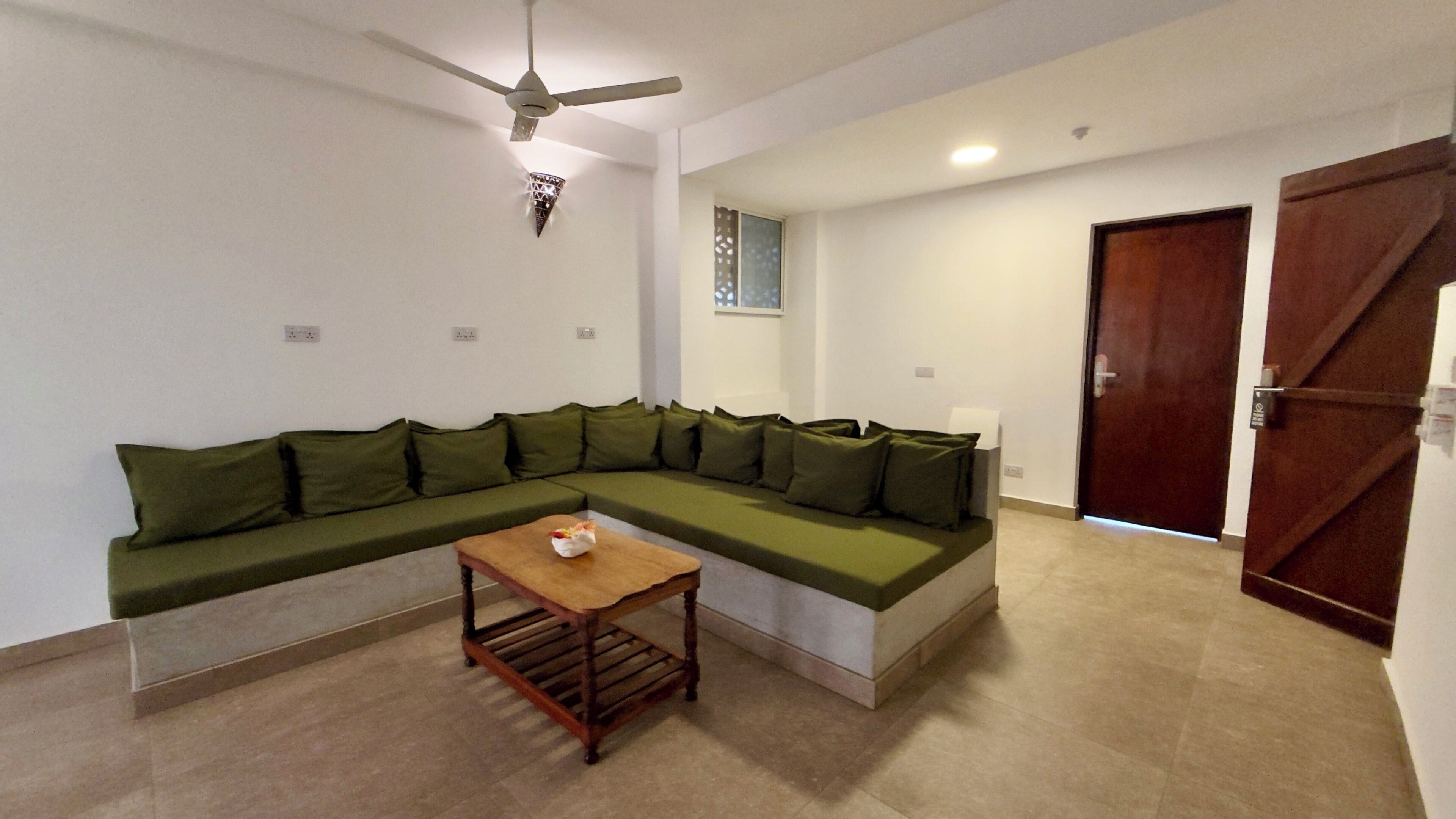A living room with a sectional sofa, a wooden coffee table, a ceiling fan, and a door.