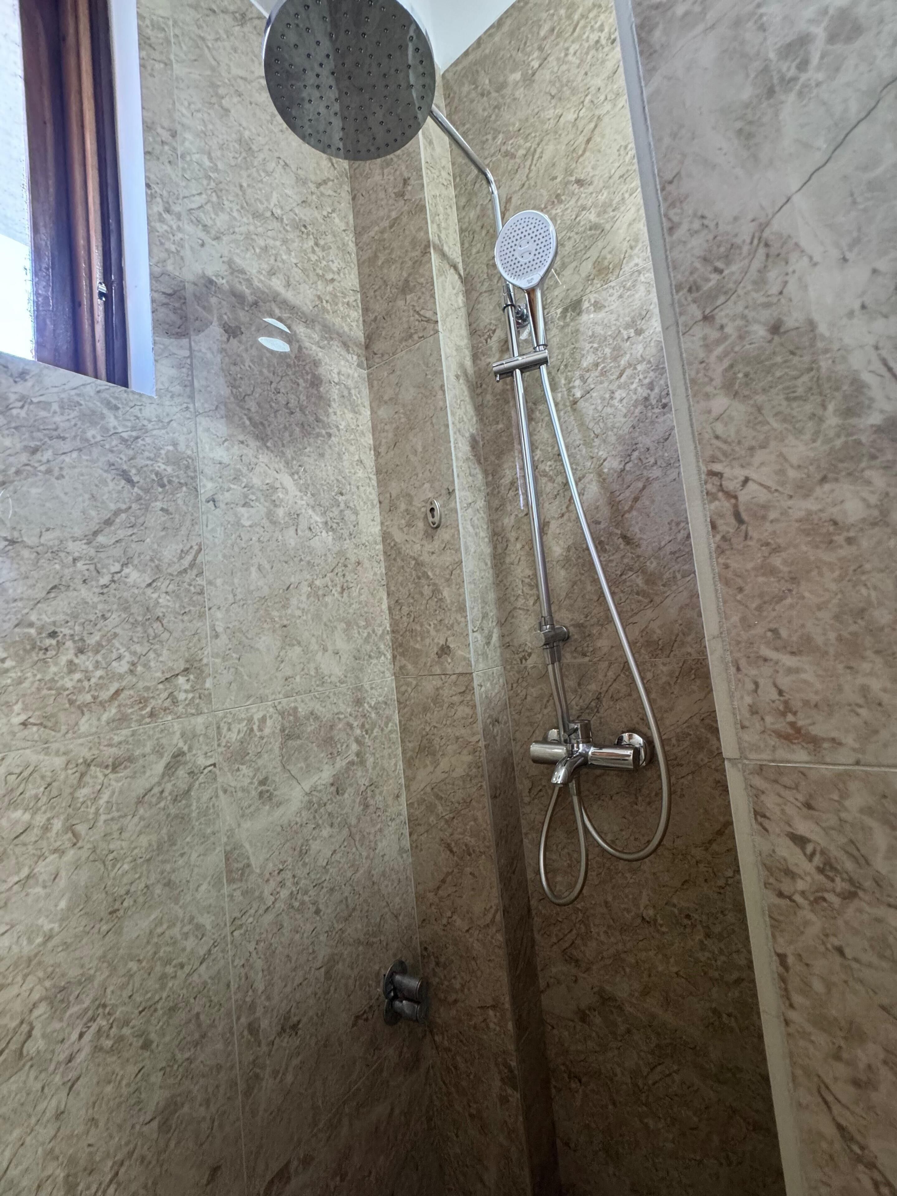 A shower with a handheld showerhead and a wall-mounted faucet in a bathroom with marble walls.