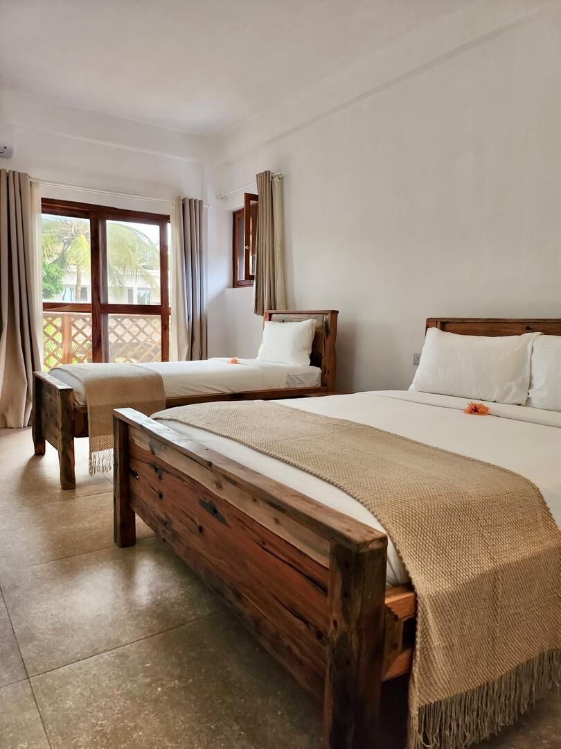 A hotel room with two wooden beds, a balcony, and a view of greenery.